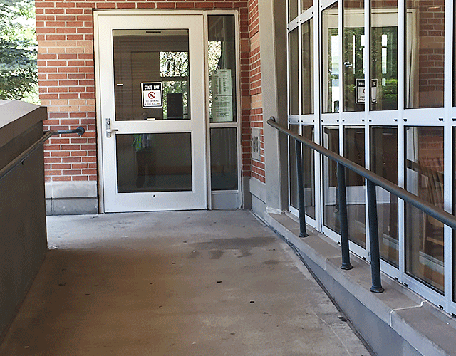 A ramp leading to a single door entrance. The door contains a no smoking sign.