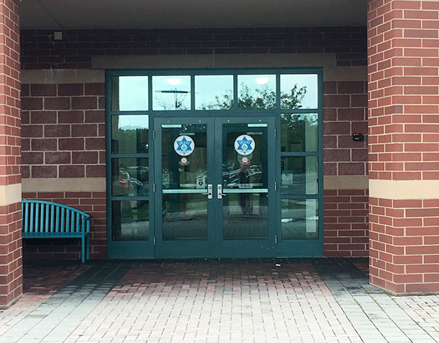 ADA-accessible entrance with signage. The double doors are accessed from the street level. To the left of the doors is a bench. 