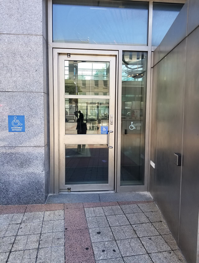 Courthouse with a single door entrance with ADA signage located on the street level. There is a push button to the right of the door on the side of the building.