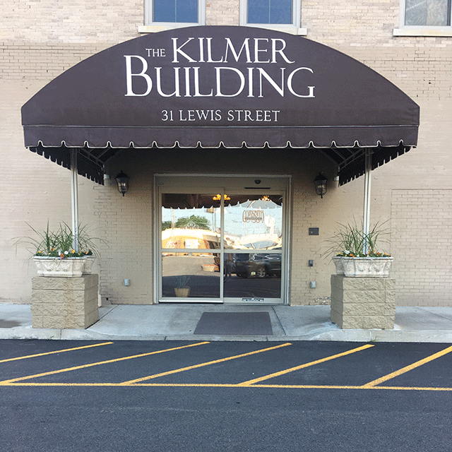 The Kilmer Building entrance has two automatic sliding doors on street level. There is an awning from the curb to the entrance. On both sides of the entrance are plant boxes.