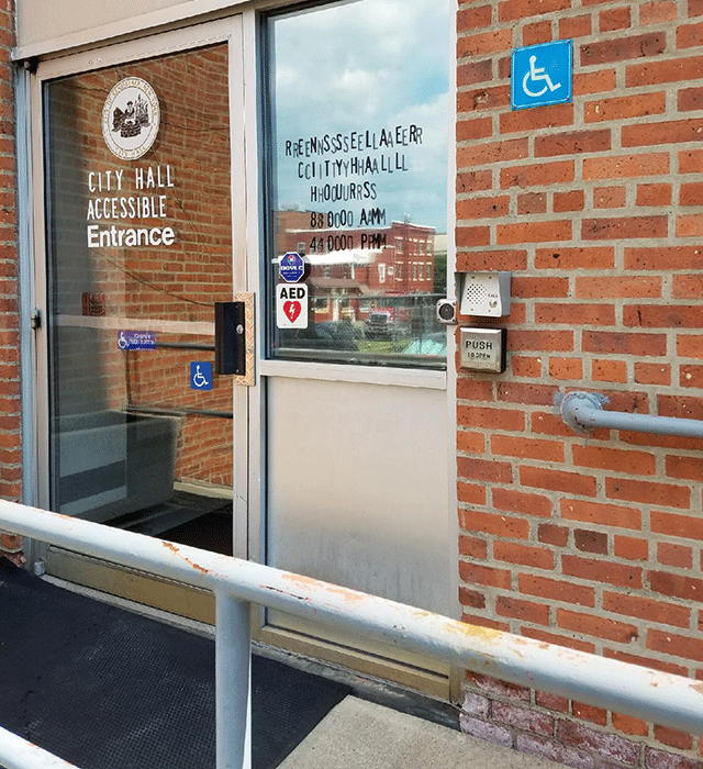 The City Hall accessible entrance with a ramp that leads to this door. There is a push button and intercom at the end of the ramp.