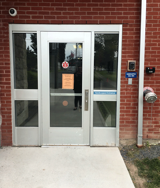 A single door entrance that is accessed from a walkway. There is a ADA sigange to the right of the door. On the right side of the building is a call box.