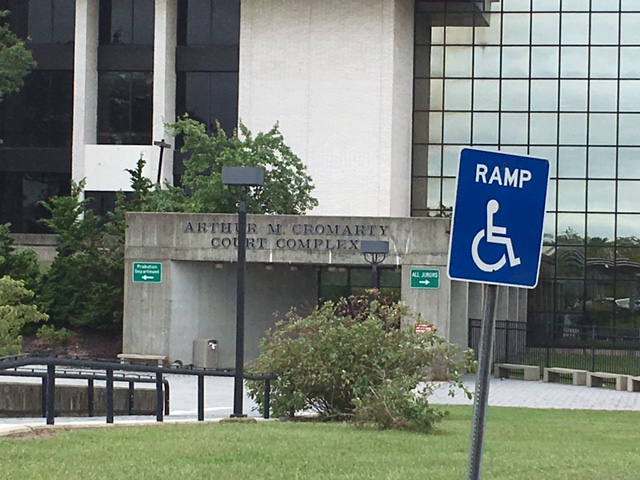 This is an angled view of the entrance of the court facility. There is a ramp toward the left and a large lawn area on the right. On the lawn there is a sign indicating there is a ramp nearby.