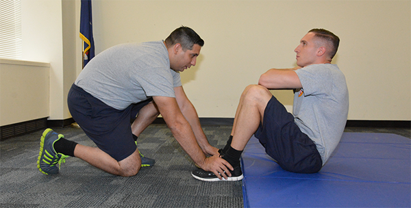 man holding other man's feet down as  he does sit ups