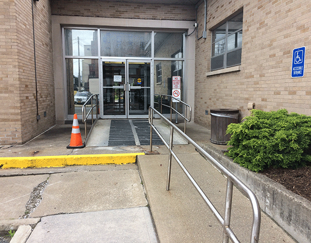 There is a ramp leading to two doors. An ADA-accessible sign is posted to the right of the ramp on the side of the building.
