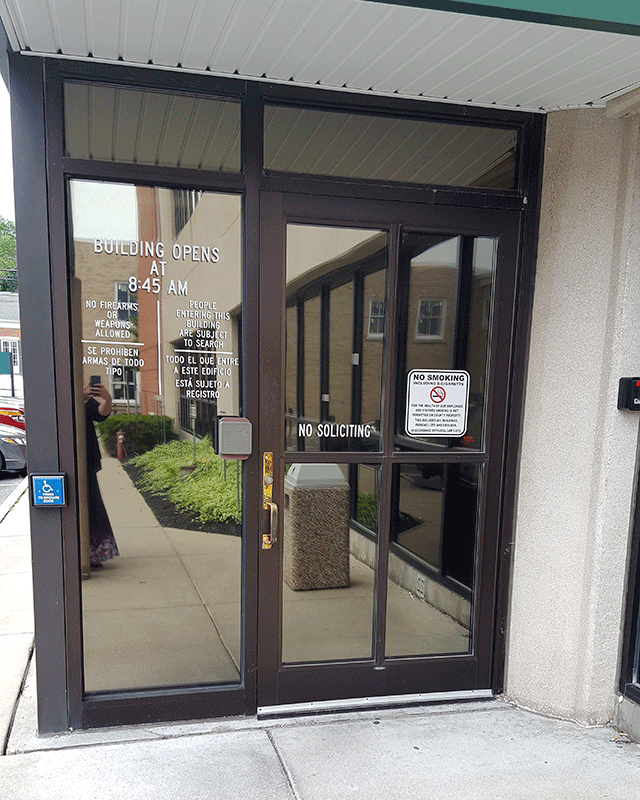 A single door entrance to the court facility that is accessed from the sidewalk. There is a push button to the right of the door connected to the building.