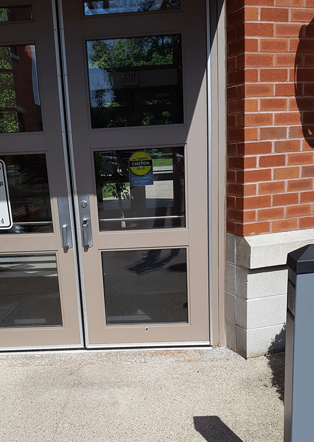 A double door entrance to the court facility. There is a pole with a push button on the right side in the walkway.