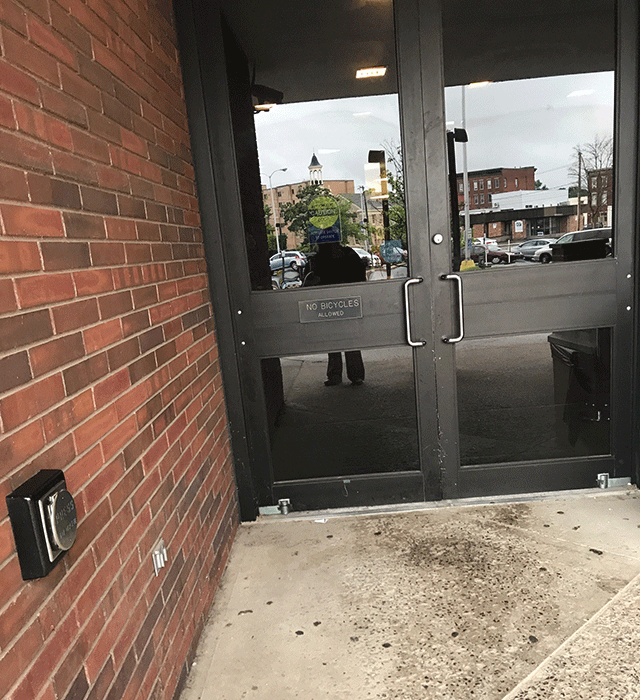 A double door entrance located on street level. There is a push button to the left of the entrance on the side of the building.