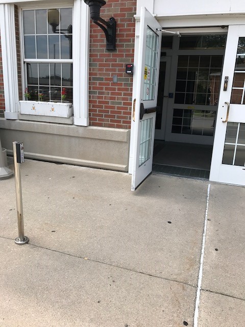 Genesee County Court Facility entrance of a  double door. The left door is open. There is a pole on the left with a push button.