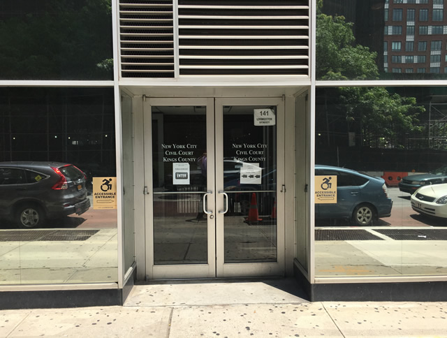 The double door entrance to Kings County Civil Court. There are ADA-accessible signs on both sides of the door both pointing toward the entry way.