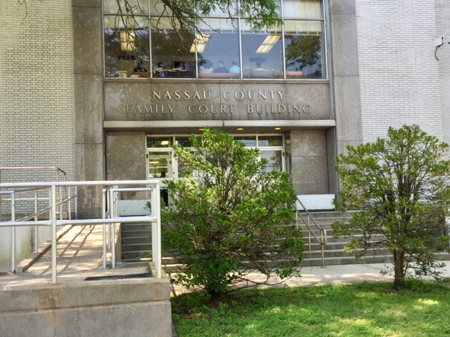 The courthouse has a ramp to the left of the entrance. There is a walkway with  a set of stairs with railings leading directly to the entrance. Behind the walkway is a lawn area with small trees.