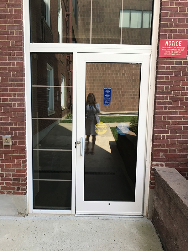 The entrance is a single white door. There is a push button to open the door to the left of the door.