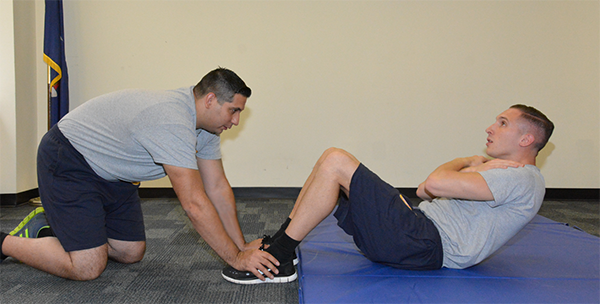 man holding other man's feet down as he does sit ups without touching mat with mid back