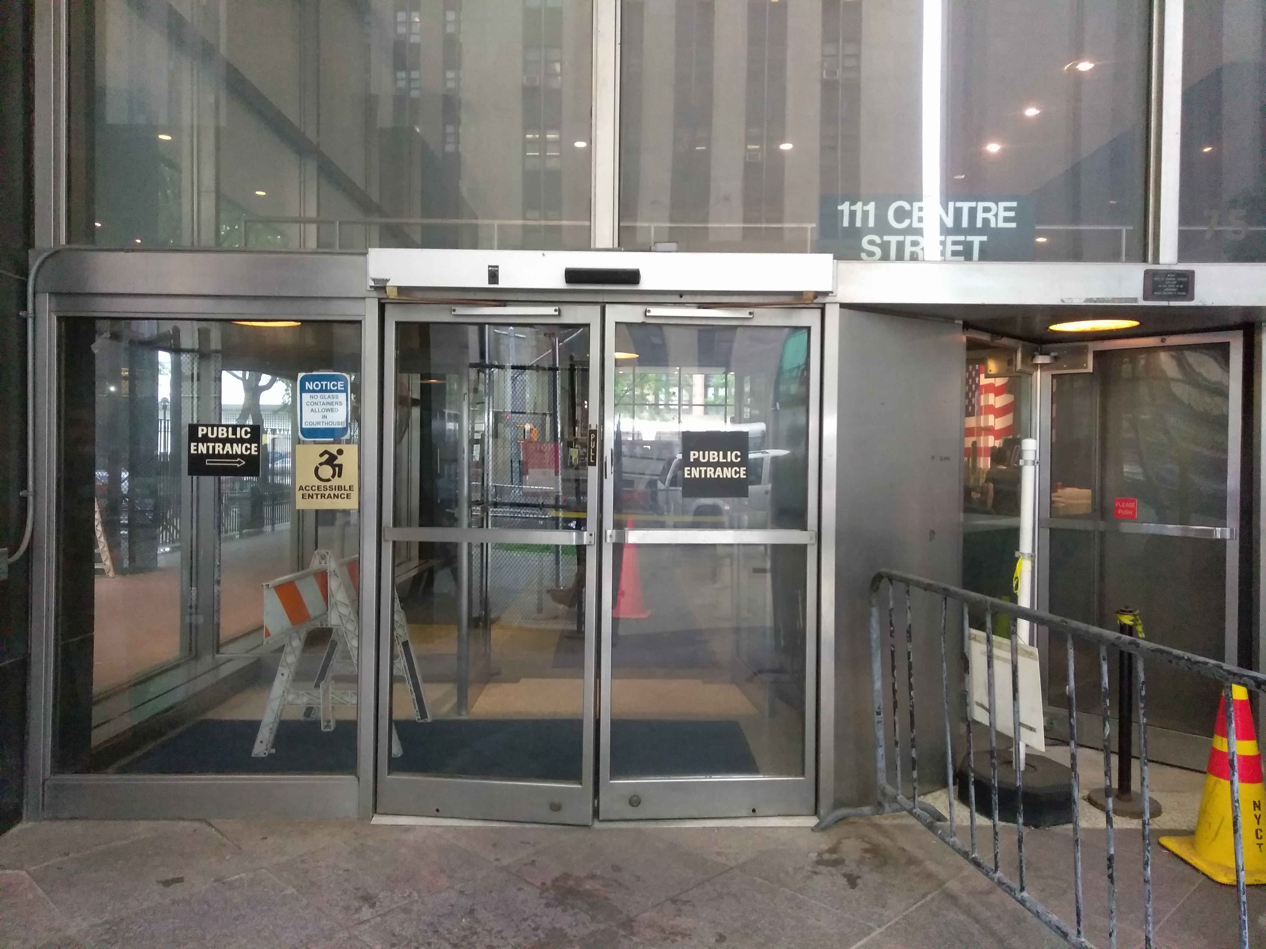A double door entrance labeled Public Entrance is located on the street level.  To the left of the double doors is ADA signage.  There is a barricade to the right of the double door entrance.