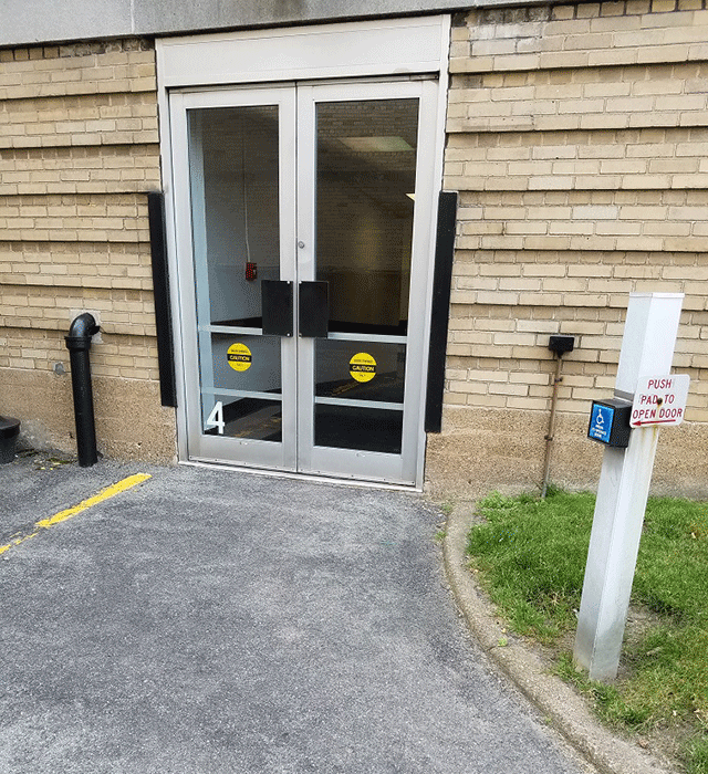 A set of doors accessed from the street. There is a pole with a push bottom to open the doors on the lawn to the right hand side.