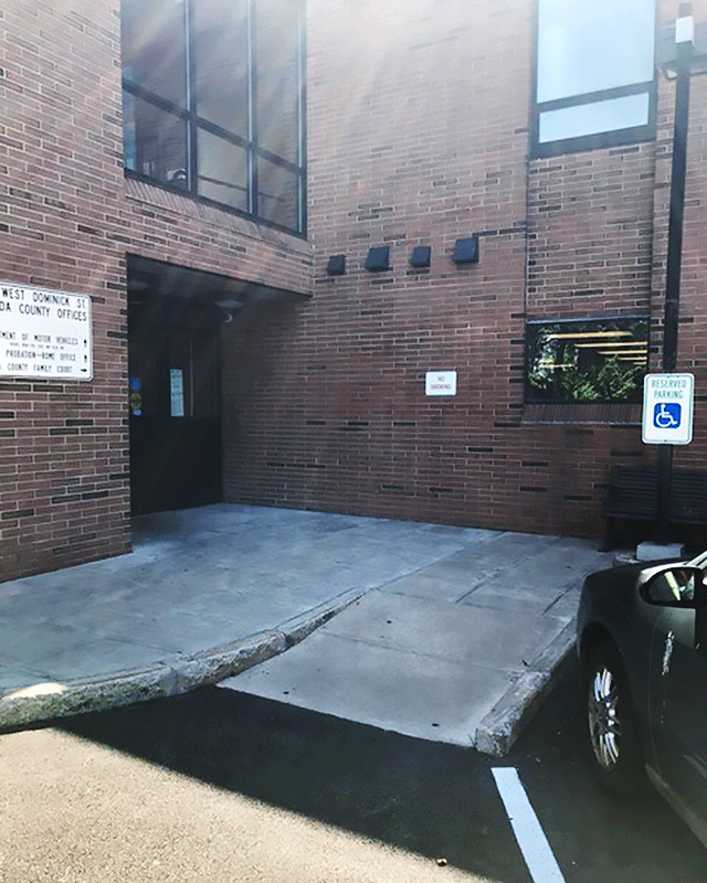 This is a photo of an entrance from a parking area. There is a sloped curb with ADA signage. The entrance is to the left of the sloped area.