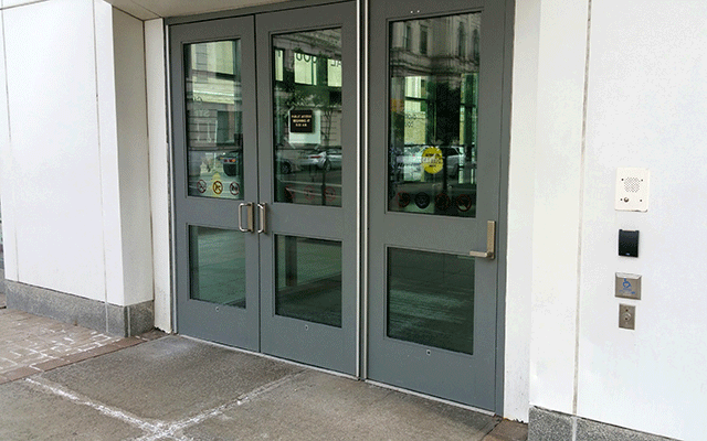 a set of double doors to the left and a single door to the right. The single door is automatic and the push button is located to the left of the door and is directly attached to the wall.