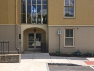 A view of the entrance with ADA signage. The entrance is located off of the side walk and has a set of double doors.