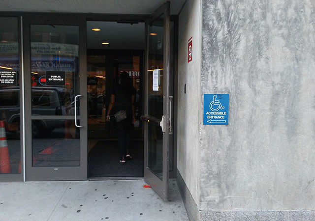 A set of double doors, the door to the right is completely open. There is ADA signage and a no smoking sign on the right side of the building.
