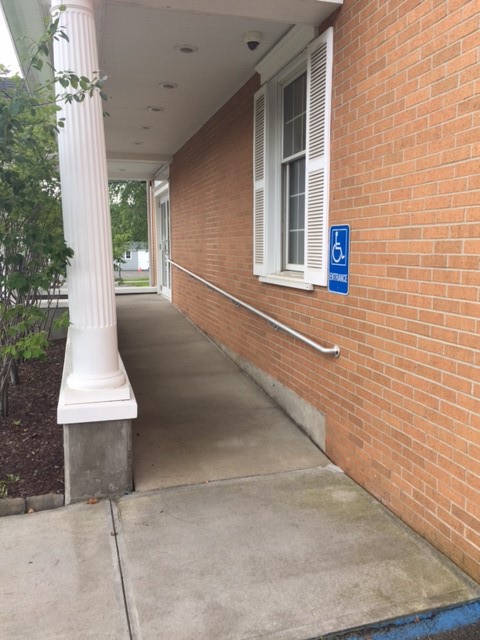A ramp lined with columns on the left side that leads to an entrance toward the right. There is signage posted on the building to the right near a window.
