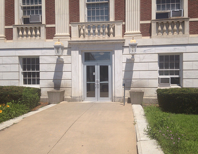 The double door entrance that is accessed from a walkway. There is a push button on a pole to the right of the doors.