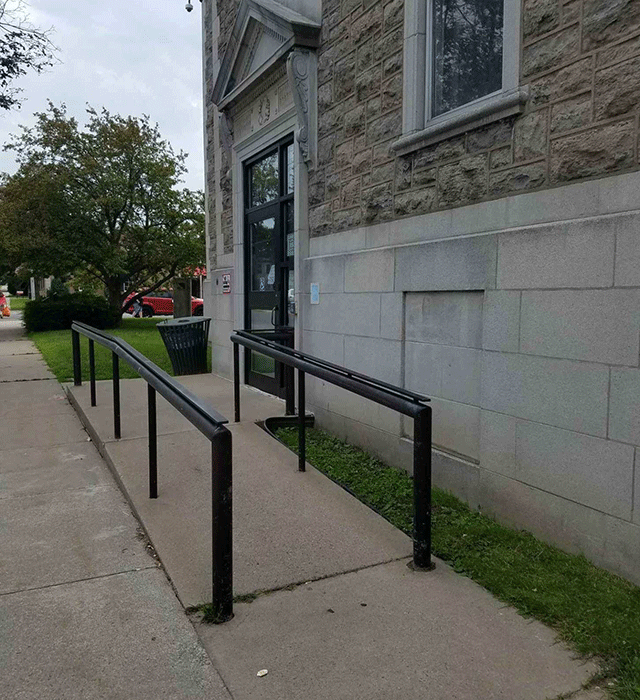 A side view of the entrance to the court facility. There is a ramp that is accessed toward the right that leads to the doors.