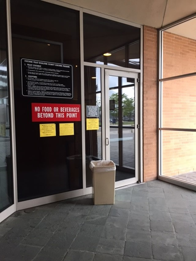 A single door to the entrance of the court facility . On the left of the door there is signage indicating there is no food or beverages allowed.