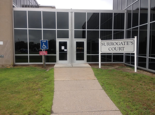 Two single door entrances to the courthouse. There is a walkway leading to the two doors with a lawn area on both sides of the walkway. There is ADA signage on the lawn on the left and a 'Surrogate's Court' sign on the right lawn.
