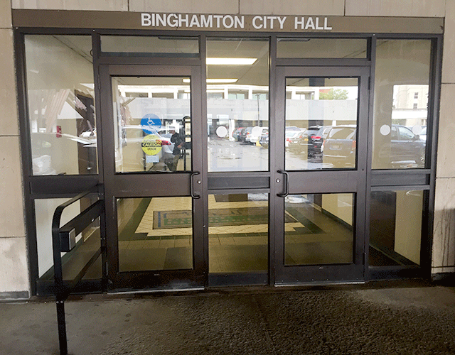 There are two single doors located at the entrance to Binghamton City Hall. There is a push button located on a railing to the left that can be pushed to open the left door.