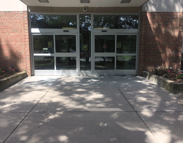 The entrance contains two sets of automatic sliding doors. The doors are on street level. There are garden areas to the left and right of the entrance.