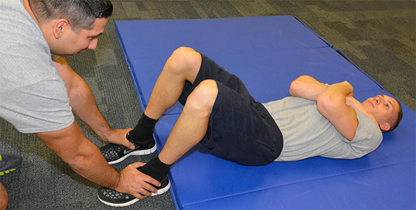 man holding other man's feet down as he does sit ups