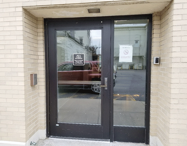 A single door that states it is not a public entrance and a no smoking sign. There is a buzzer on the left adjacent wall and a bell toward the far right side of the door.