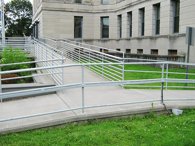 The courthouse is in the background. There is a ramp to the left and right of the grassy area that connect to form a single ramp that leads to the entrance.