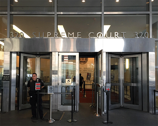Two revolving doors divided by a ADA-accessible double door. The doors are located on street level. The double door has ADA signage. There is a court officer in the photo in front of the revolving doors to the left.