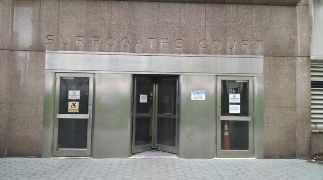 The entrance to Surrogate's Court accessed from street level. There is are two single doors on each side of the entry way with a revolving door in the center. There is ADA signage on the single door toward the left.