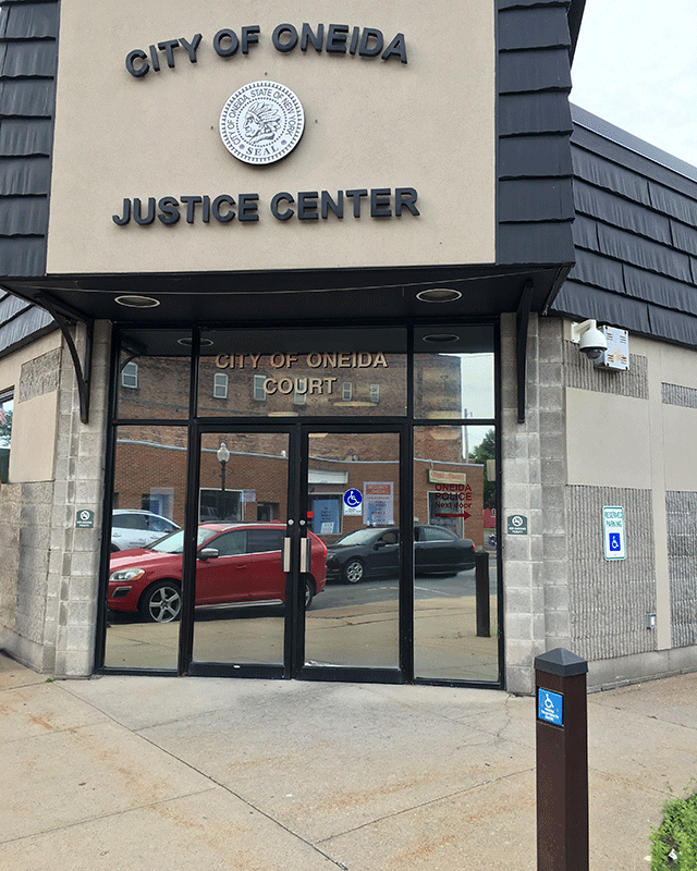 The entrance to the City Court of Oneida has two mirrored doors located that are accessed from the sidewalk. There is a push button closer to the curb on the right side. There is ADA-accessible signage on the right door, on the side of the building, and on the push button.