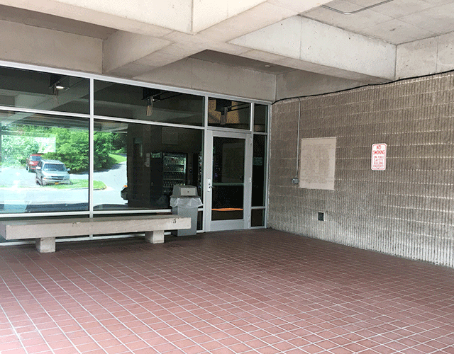 The courthouse has a single door to the right. On the left is a garbage pail and a bench.