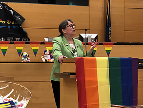 Judge speaking at podium with rainbow flag