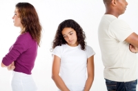 Sad child standing between her parents who are angry with one another