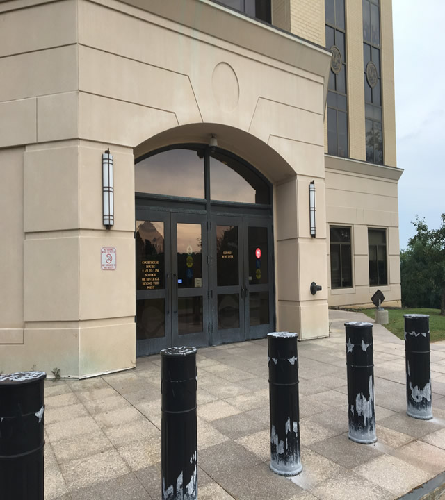 The photo shows two sets of double doors that are accessed from the sidewalk. Lining the entrance area are large black poles.